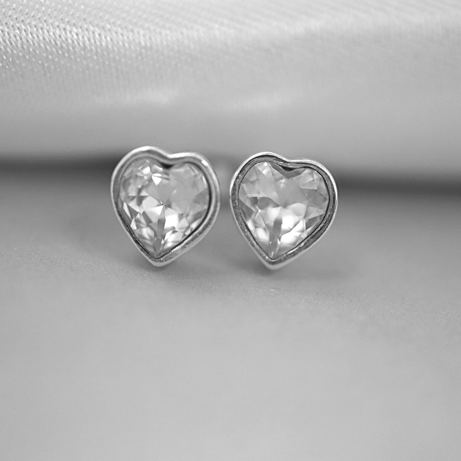 Heart-shaped silver earrings on a textured white and gray surface