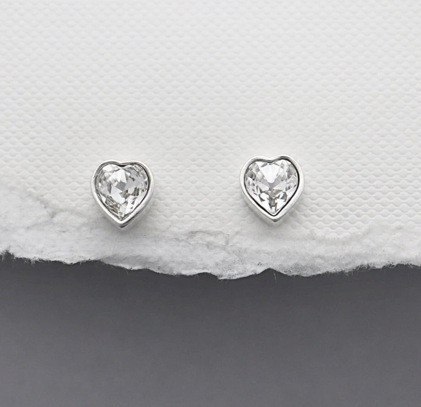 Heart-shaped silver earrings on a textured white and gray surface