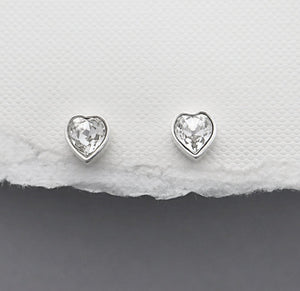 Heart-shaped silver earrings on a textured white and gray surface
