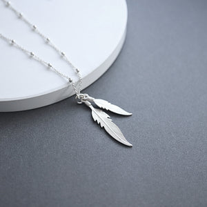 Silver feather necklace on a gray surface with a white circular object in the background