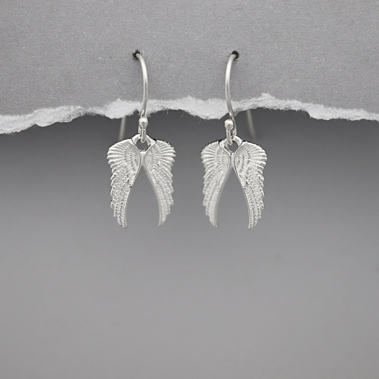 Silver angel wing earrings on a gray background