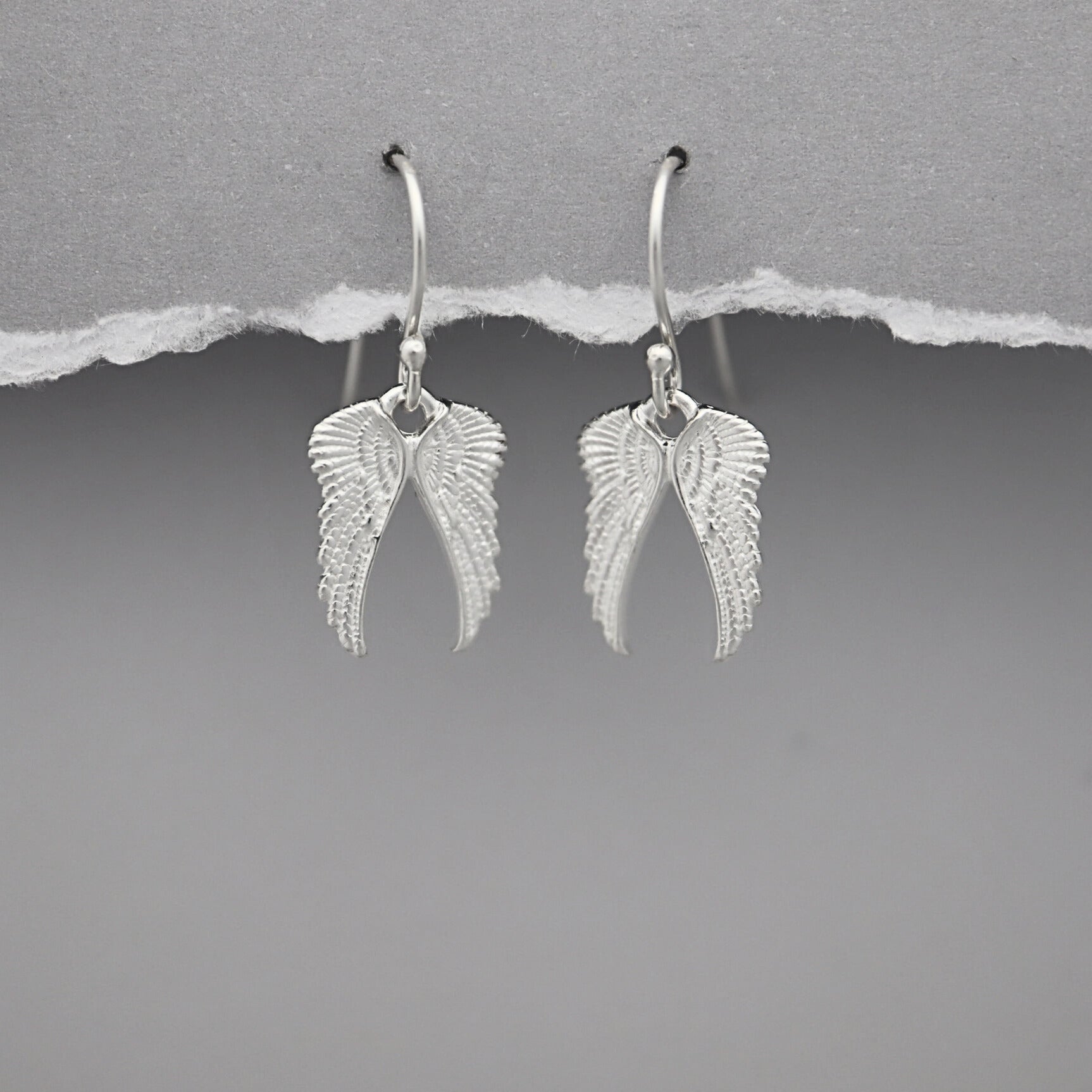 Silver angel wing earrings on a gray background