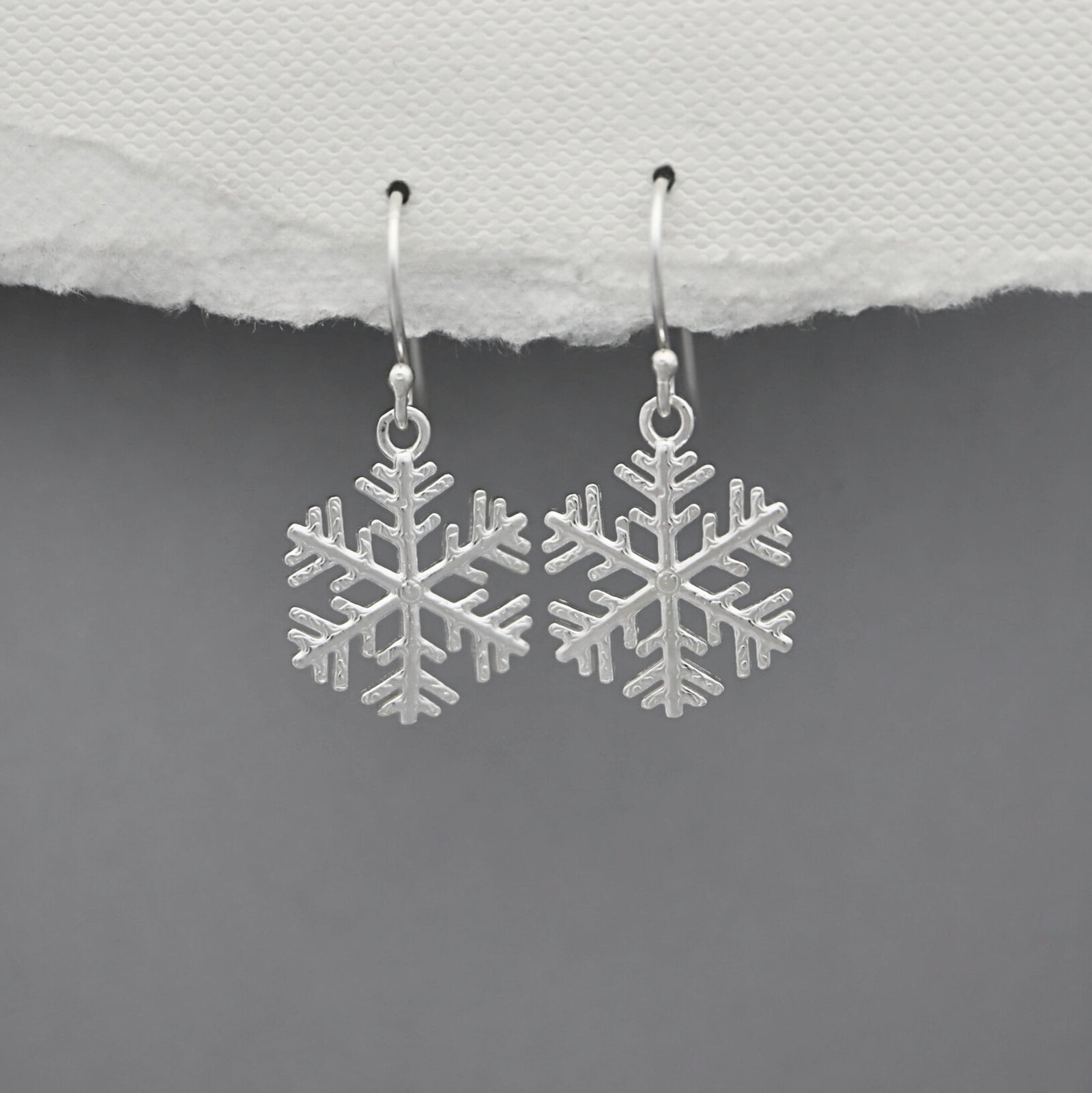 Silver snowflake earrings on a gray background