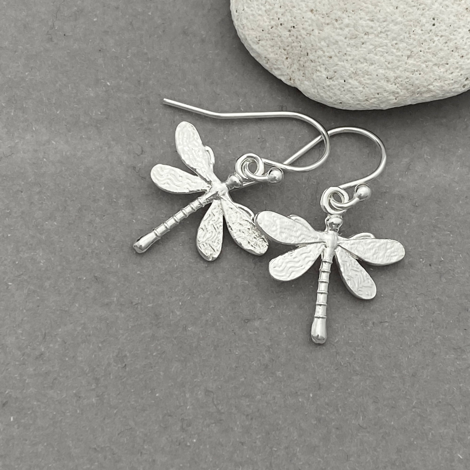 Silver dragonfly earrings on a gray surface with a stone in the background