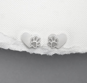 Heart-shaped silver earrings with paw prints on a white fabric background