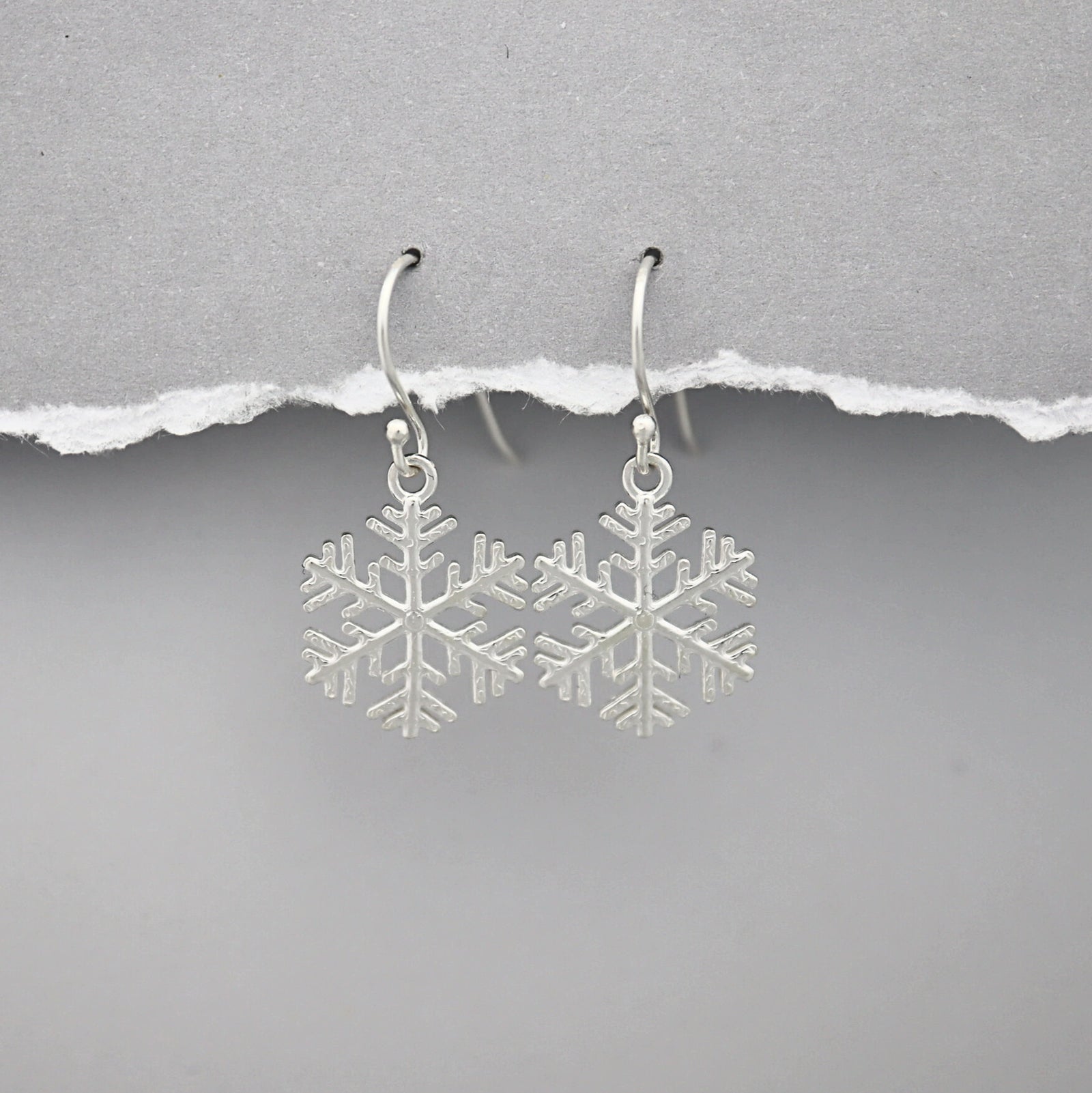 Silver snowflake earrings on a gray background
