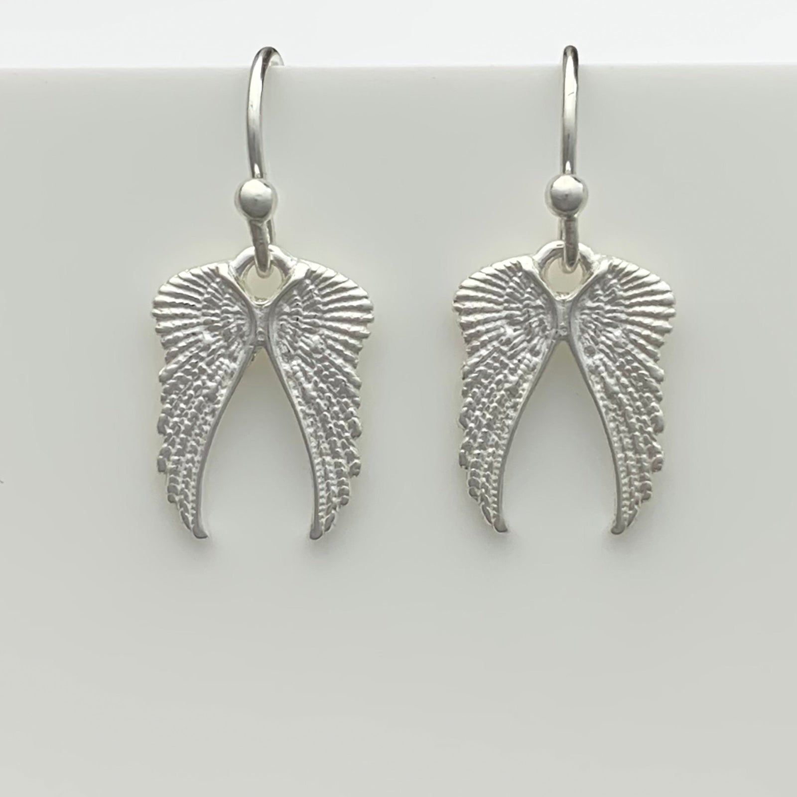 Silver angel wing earrings on a gray background
